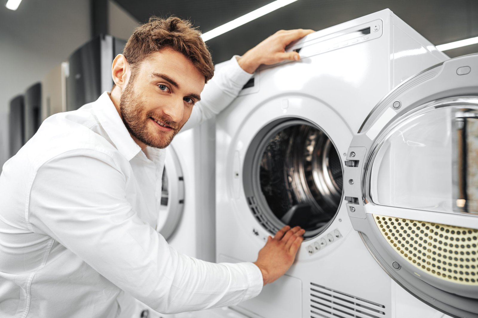 young man choosing new washing machine in household appliances store